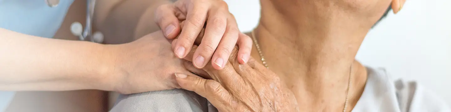 Pflegerin drückt die Hand einer älteren Patientin auf ihrer Schulter