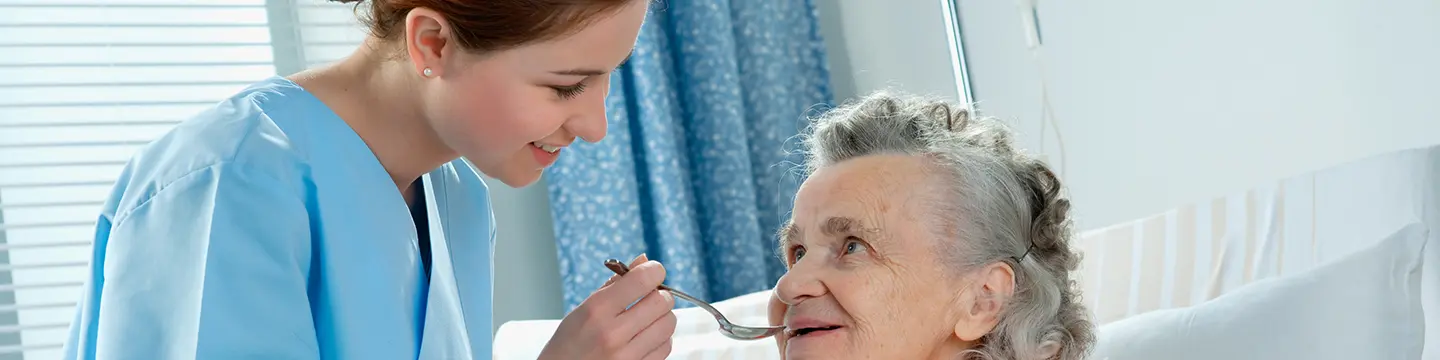 Pflegekraft füttert ältere Dame mit einen Löffel