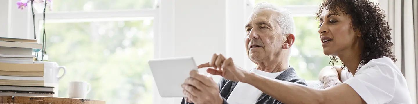 Pflegerin hilft Senior bei Tablet-Nutzung