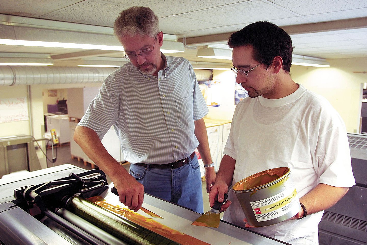 Foto: Ein älterer Herr erklärt einem jungen Mann, wie man eine Druckmaschine einstellt
