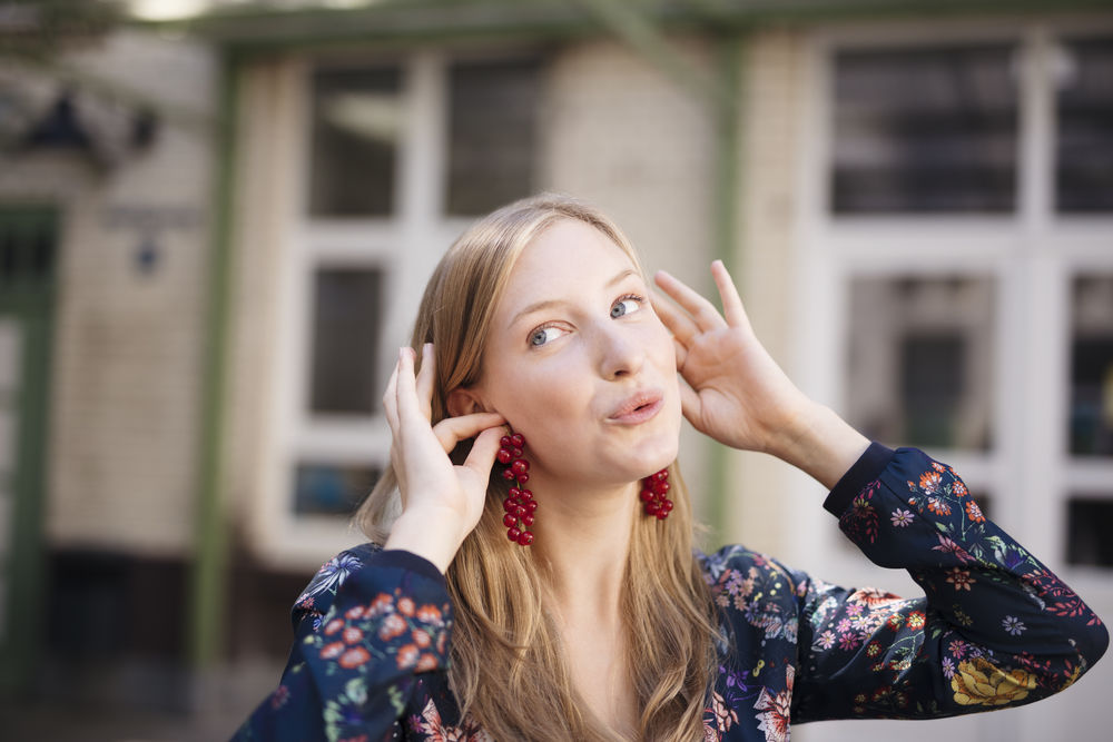 Eine junge Frau steht hält sich Johannisbeeren als Ohrringe an die Ohren.