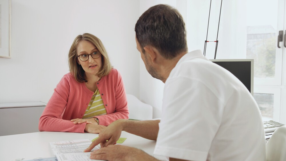 Eine Frau sitzt vor einem Arzt. Gemeinsam besprechen sie medizinische Werte.