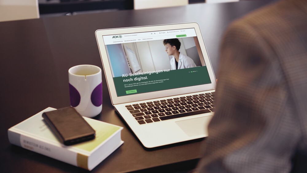 Blick geht von hinten über die Schulter einer Person auf den Laptop-Bildschirm, der eine Info zur elektronischen AU-Bescheinigung zeigt. 