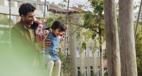 Mann hält ein kleines Mädchen fest, das auf einer Schaukel steht. 