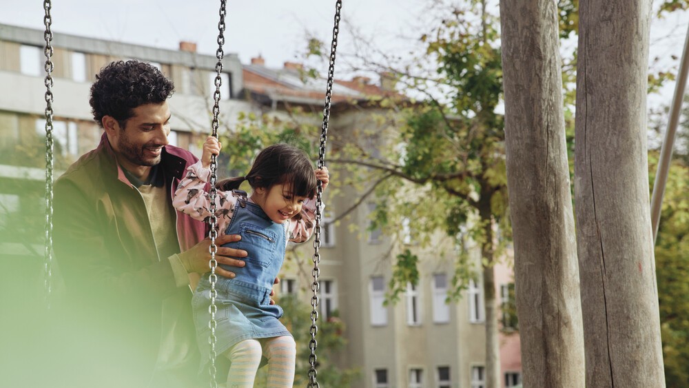 Mann hält ein kleines Mädchen fest, das auf einer Schaukel steht. 