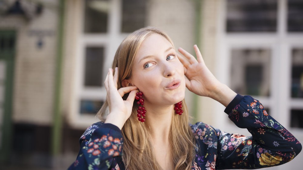Eine junge Frau steht hält sich Johannisbeeren als Ohrringe an die Ohren.