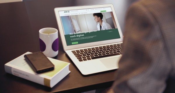 Blick geht von hinten über die Schulter einer Person auf den Laptop-Bildschirm, der eine Info zur elektronischen AU-Bescheinigung zeigt.