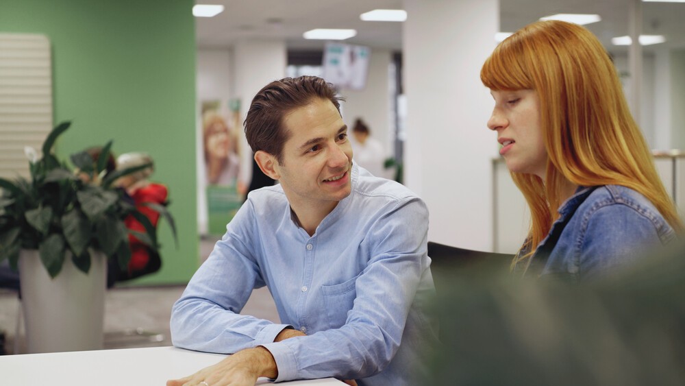 In einem AOK-KundenCenter sind ein Mann und eine Frau bei der Beratung zu sehen.