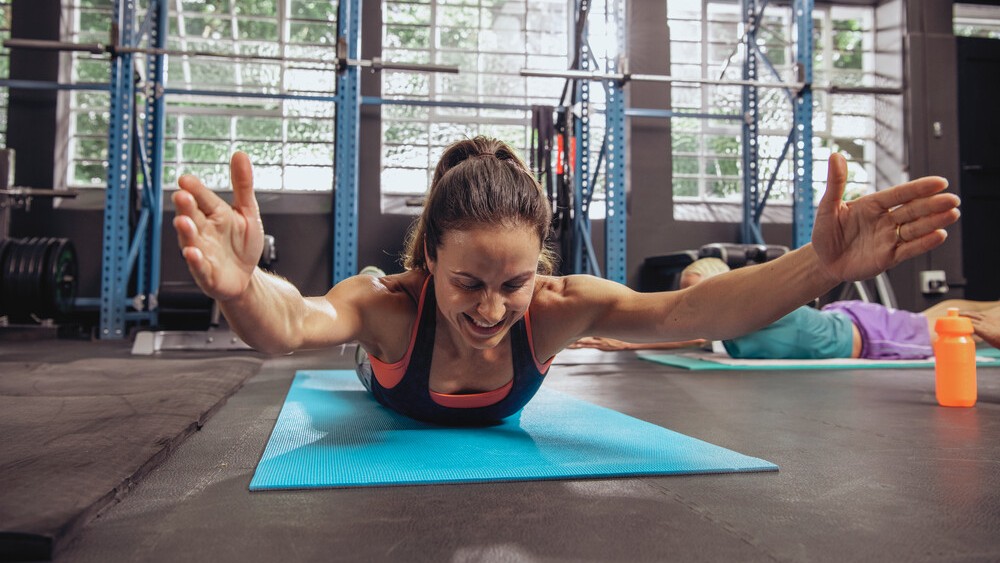Frau liegt auf einer Matte auf dem Bauch. Sie macht eine Rückenübung.