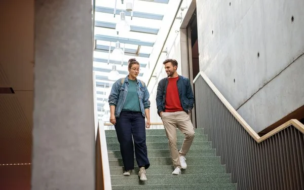 Eine Frau und ein Mann gehen eine Treppe hinunter und unterhalten sich dabei miteinander.