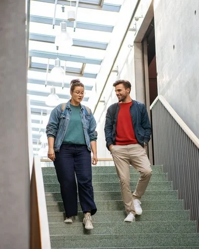 Eine Frau und ein Mann gehen eine Treppe hinunter und unterhalten sich dabei miteinander.