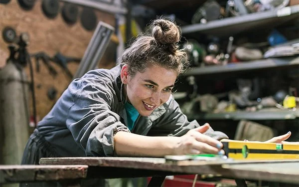 Junge Handwerkerin misst mit einer Wasserwaage ein Werkstück in der Werkstatt.