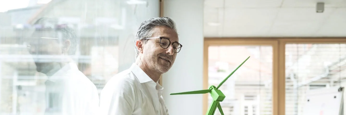 Ein Mann hält ein Miniaturwindkraftwerk in der Hand. 