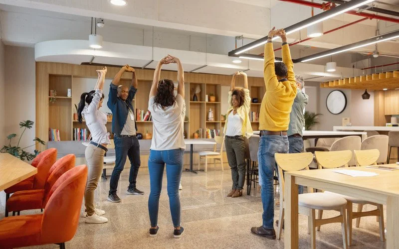 Mehrere Beschäftigte stehen im Büro im Kreis und machen gemeinsam eine Streckübung.