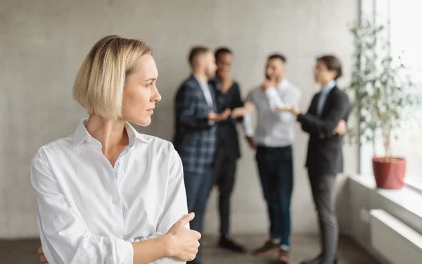 Eine Frau im Büro fühlt sich von einem Viererteam beobachtet.