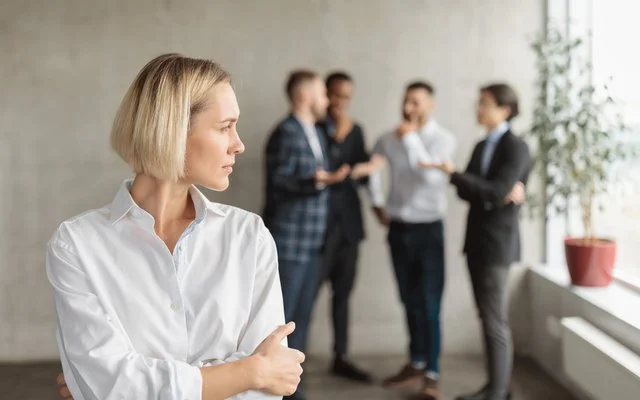 Eine Frau im Büro fühlt sich von einem Viererteam beobachtet.