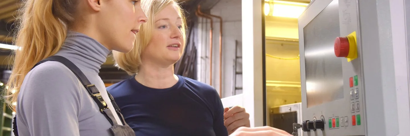 In einem Produktionsbetrieb. Eine Kollegin erläutert einer anderen etwas an einem Monitor.