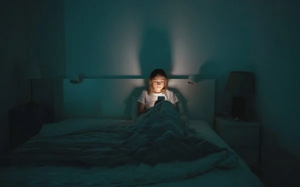 Eine Frau liegt im Bett und schaut aufs Handy.