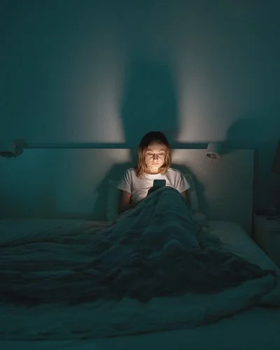 Eine Frau liegt im Bett und schaut aufs Handy.