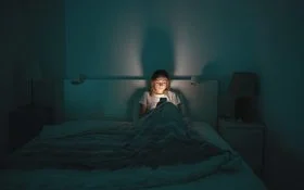 Eine Frau liegt im Bett und schaut aufs Handy.