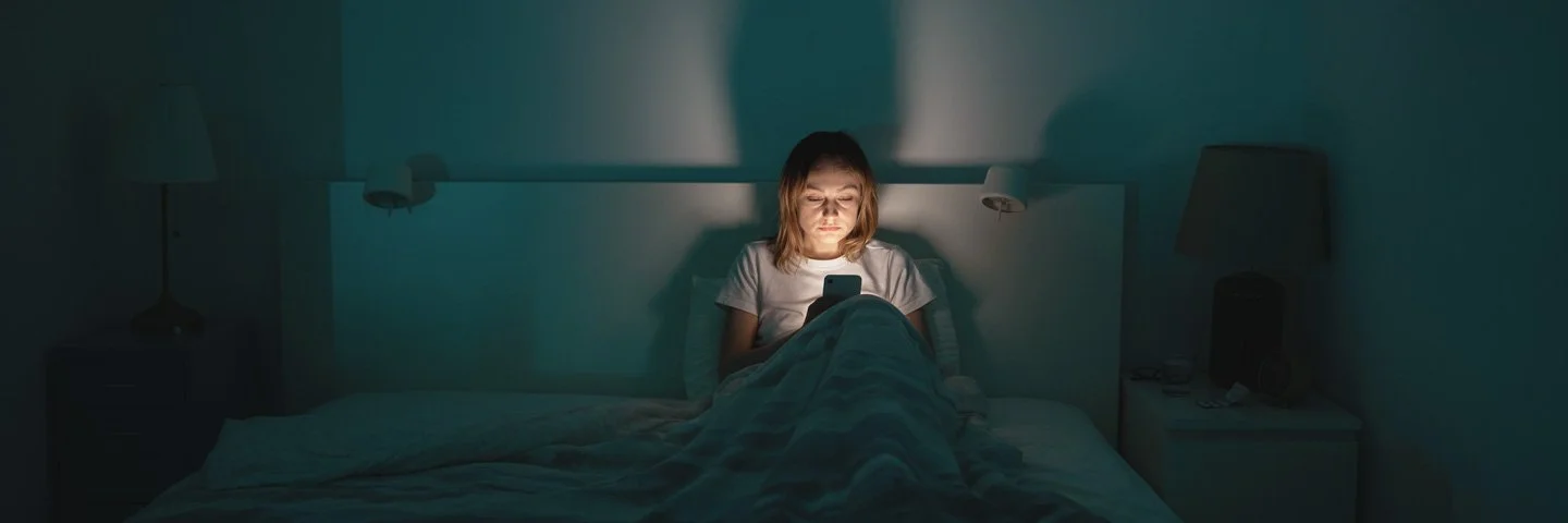 Eine Frau liegt im Bett und schaut aufs Handy.