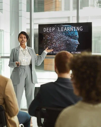 Eine Frau hält ein Seminar und erklärt den Teilnehmenden Inhalte an einer digitalen Tafel.