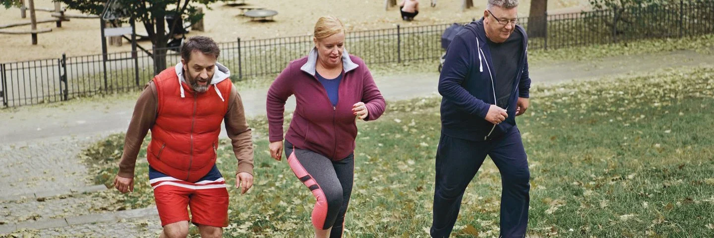 Drei Menschen in Sportkleidung laufen beim Trainieren im Park eine Treppe hoch.