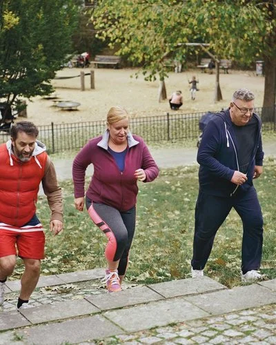 Drei Menschen in Sportkleidung laufen beim Trainieren im Park eine Treppe hoch.