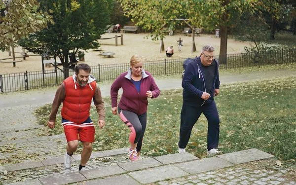 Drei Menschen in Sportkleidung laufen beim Trainieren im Park eine Treppe hoch.