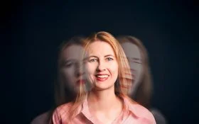 Eine Frau lacht in die Kamera. Auf ihren Schultern ihr Gesicht, wie es einmal traurig schaut und einmal schreit.