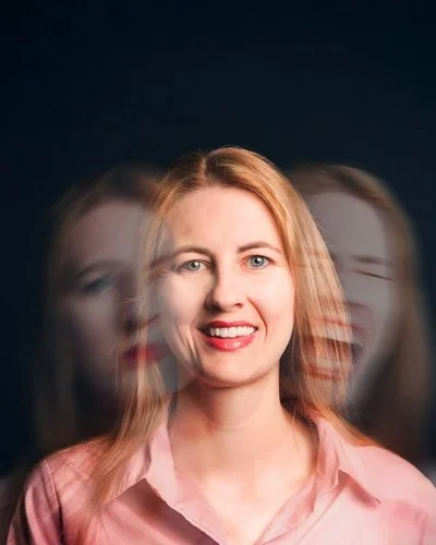 Eine Frau lacht in die Kamera. Auf ihren Schultern ihr Gesicht, wie es einmal traurig schaut und einmal schreit.