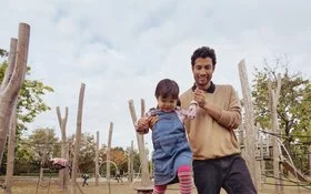 Ein Mann hält seine kleine Tochter auf dem Spielplatz beim Blancieren an den Händen fest