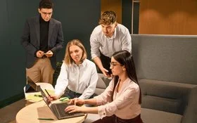 Vier Mitarbeitende im Gespräch am Laptop.