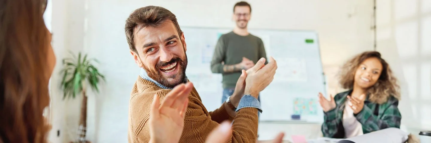 Eine Gruppe von Menschen applaudiert und lacht in einem Konferenzraum während eines Meetings