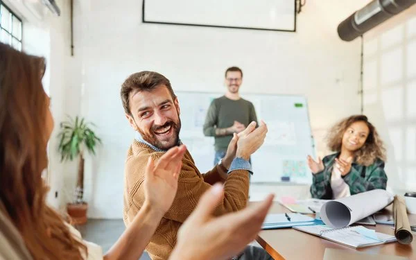 Eine Gruppe von Menschen applaudiert und lacht in einem Konferenzraum während eines Meetings