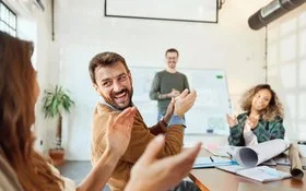 Eine Gruppe von Menschen applaudiert und lacht in einem Konferenzraum während eines Meetings