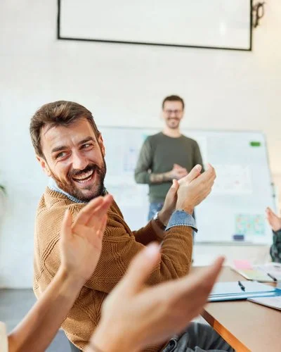 Eine Gruppe von Menschen applaudiert und lacht in einem Konferenzraum während eines Meetings