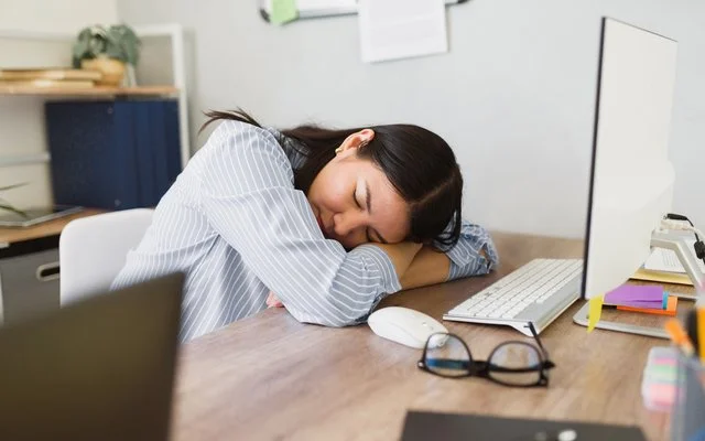 Mitarbeiterin ruht kurz am Arbeitsplatz – Symbolbild für Erholung und gesunden Schlaf im Arbeitsalltag