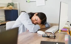 Mitarbeiterin ruht kurz am Arbeitsplatz – Symbolbild für Erholung und gesunden Schlaf im Arbeitsalltag