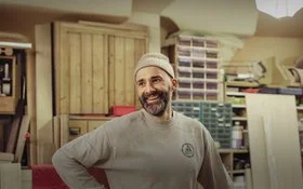 Ein Mann steht in einer Werkstatt und lacht