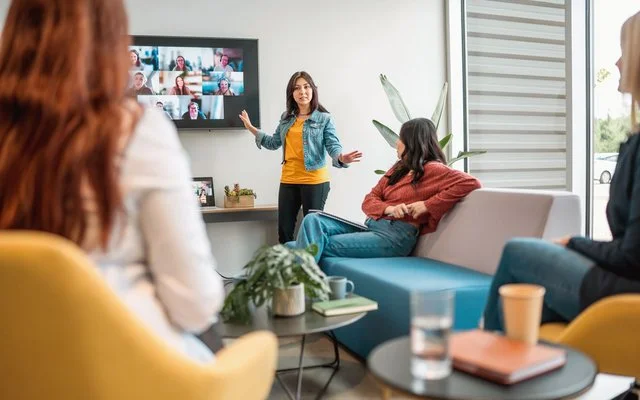 Mitarbeitende vor einem großen Bildschirm mit Videokonferenz