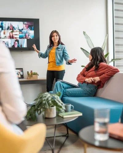 Mitarbeitende vor einem großen Bildschirm mit Videokonferenz