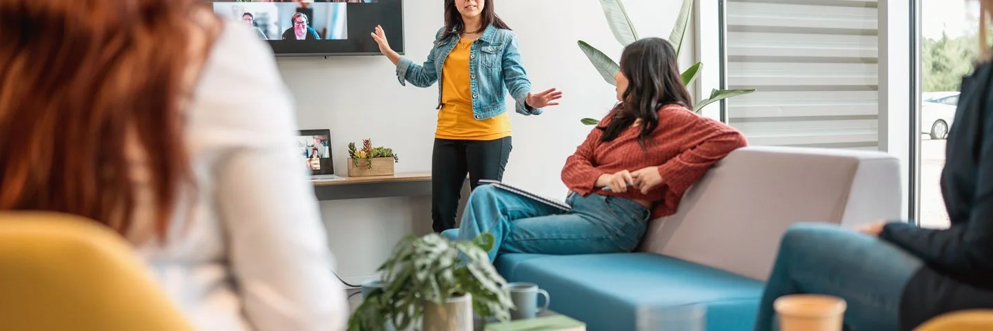 Mitarbeitende vor einem großen Bildschirm mit Videokonferenz