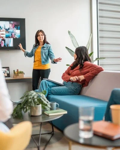 Mitarbeitende vor einem großen Bildschirm mit Videokonferenz