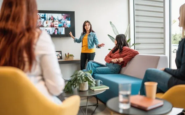 Mitarbeitende vor einem großen Bildschirm mit Videokonferenz