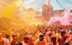 Eine Menschenmenge feiert das Holi-Festival mit buntem Farbnebel in Gelb und Pink, die Feiernden strecken ihre Arme in die Luft