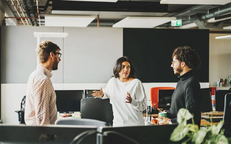 Drei Beschäftigte stehen im Büro und unterhalten sich miteinander.