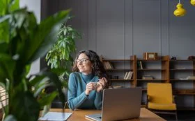 Eine Frau sitzt entspannt im Büro und schaut lächelnd aus dem Fenster