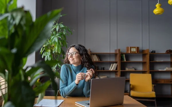 Eine Frau sitzt entspannt im Büro und schaut lächelnd aus dem Fenster