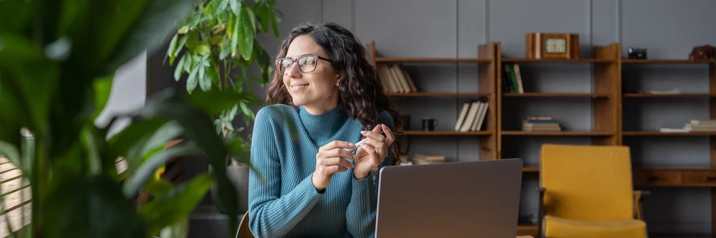 Eine Frau sitzt entspannt im Büro und schaut lächelnd aus dem Fenster